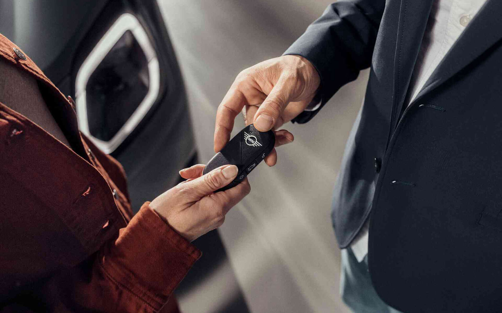 Serviceberater übergibt einer Kundin einen MINI-Fahrzeugschlüssel.