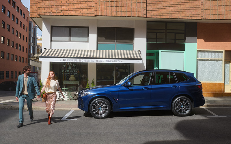 Blauer BMW SUV vor Konditorei mit Paar auf Gehweg