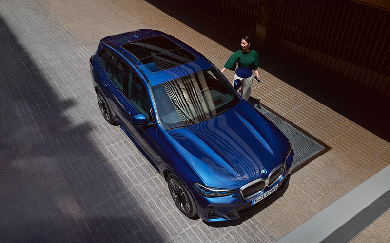 Blauer BMW SUV von oben mit Frau daneben