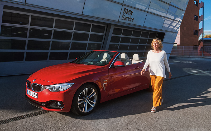 Rotes BMW Cabrio vor BMW Service Gebäude mit Frau daneben