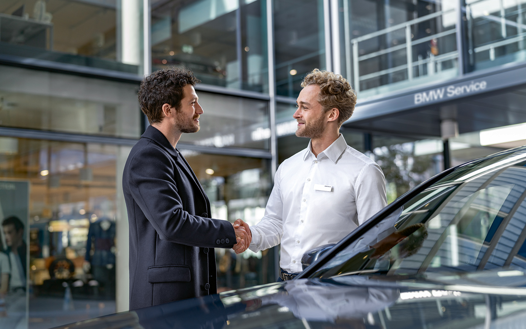 BMW Serviceberater und Kunde geben sich neben einem Fahrzeug die Hand.